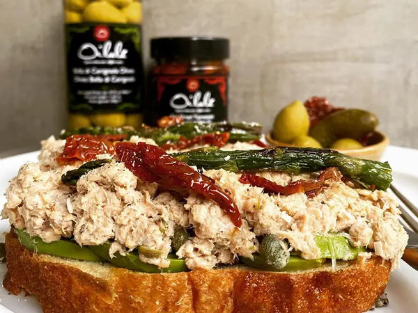 Mit Thunfisch und Antipasti belegtes Brot, im Hintergrund eingelegte Oliven und getrocknete Tomaten von Oilala
