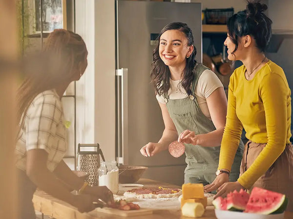 Gruppe von 3 Freundinnen bereitet gemeinsam eine Pizza und Obst zu
