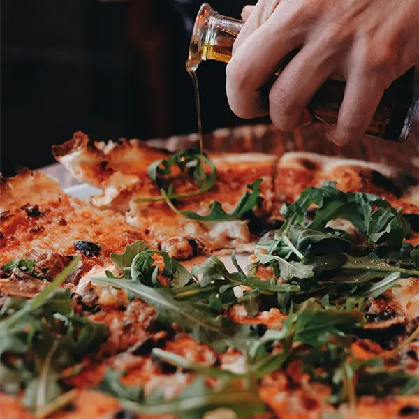 Person giesst polyphenolhaltiges olivenöl auf Pizza